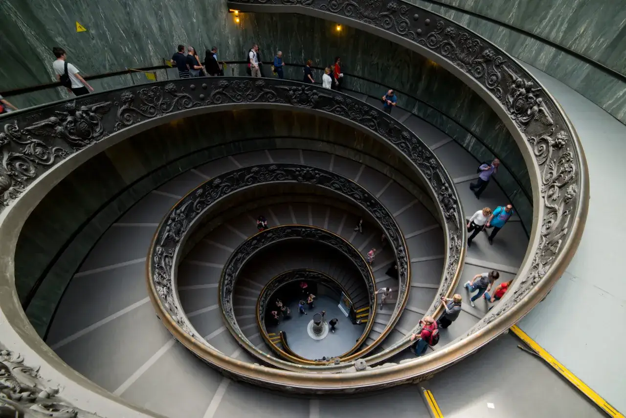 Schody w Muzeum Watykańskim, gdzie turyści z biletami podziwiają architekturę.