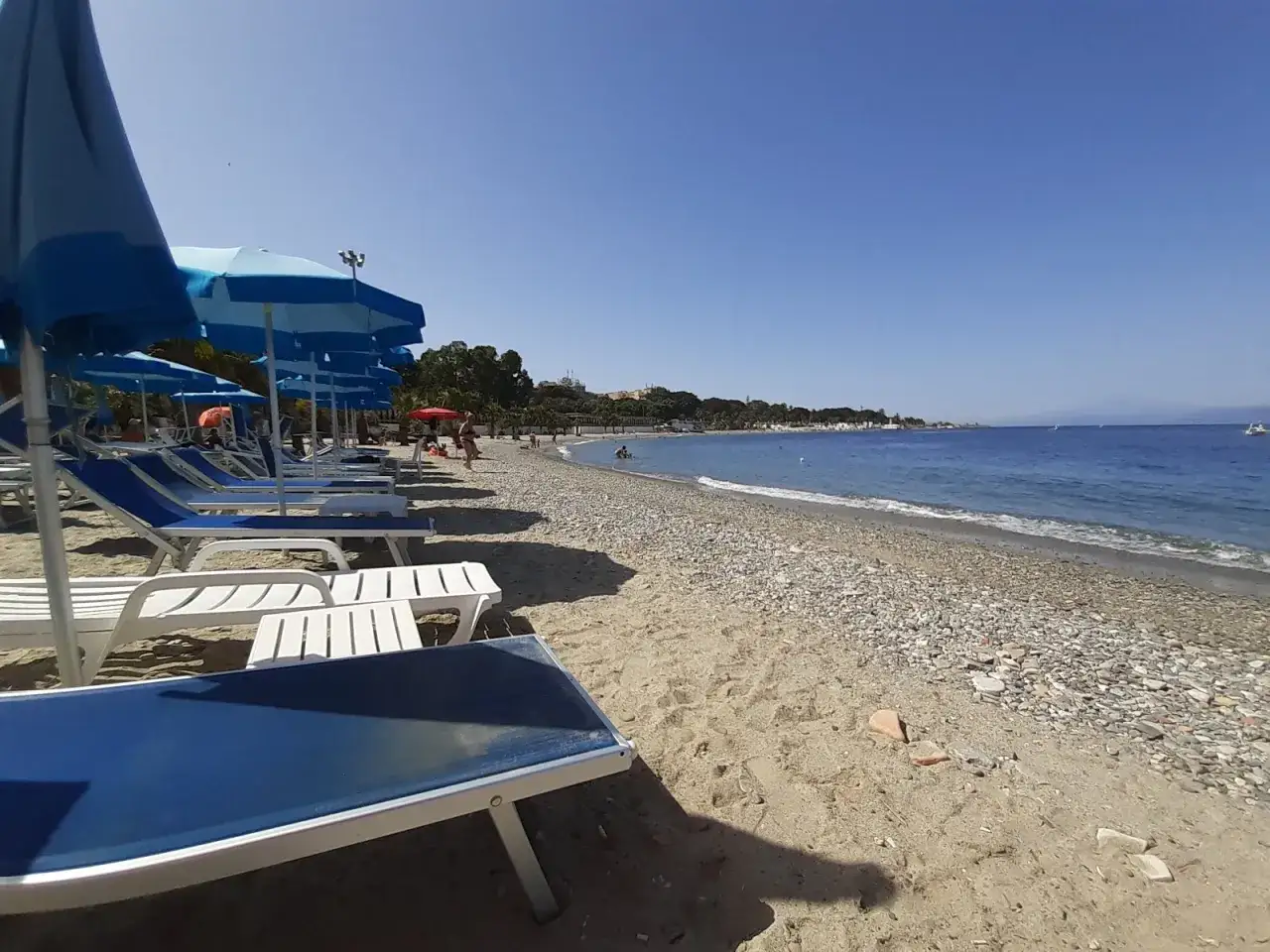 Słoneczna plaża w Reggio di Calabria z rzędami leżaków i parasoli. Błękitne morze i kamieniste wybrzeże.