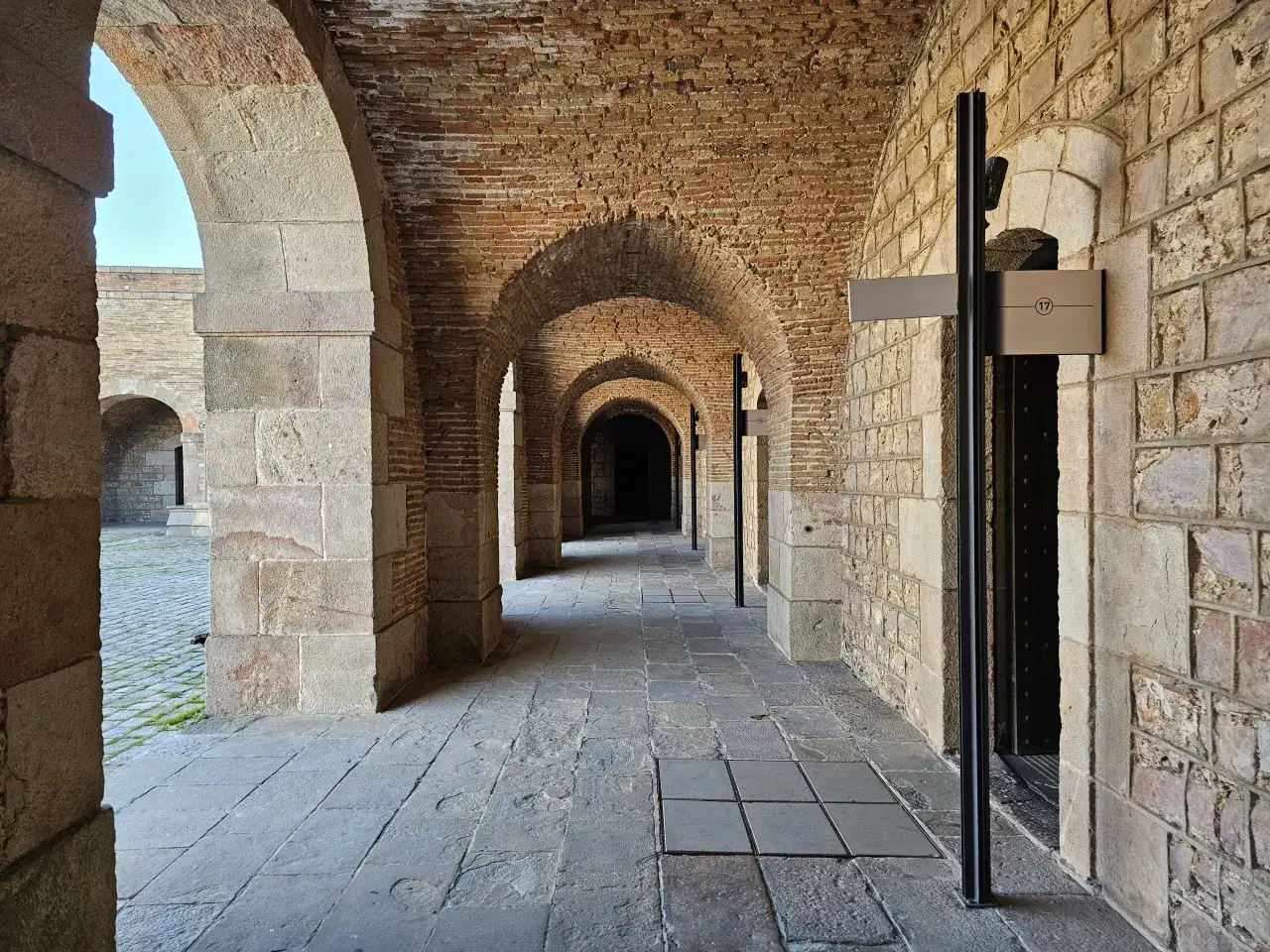 Kamienne arkady i ceglane sklepienia w zamku Castell de Montjuïc tworzą mroczny korytarz.