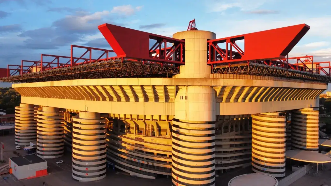Stadion Interu Mediolan w złotym świetle zachodzącego słońca. Charakterystyczne czerwone elementy konstrukcji i betonowe filary tworzą imponujący widok.