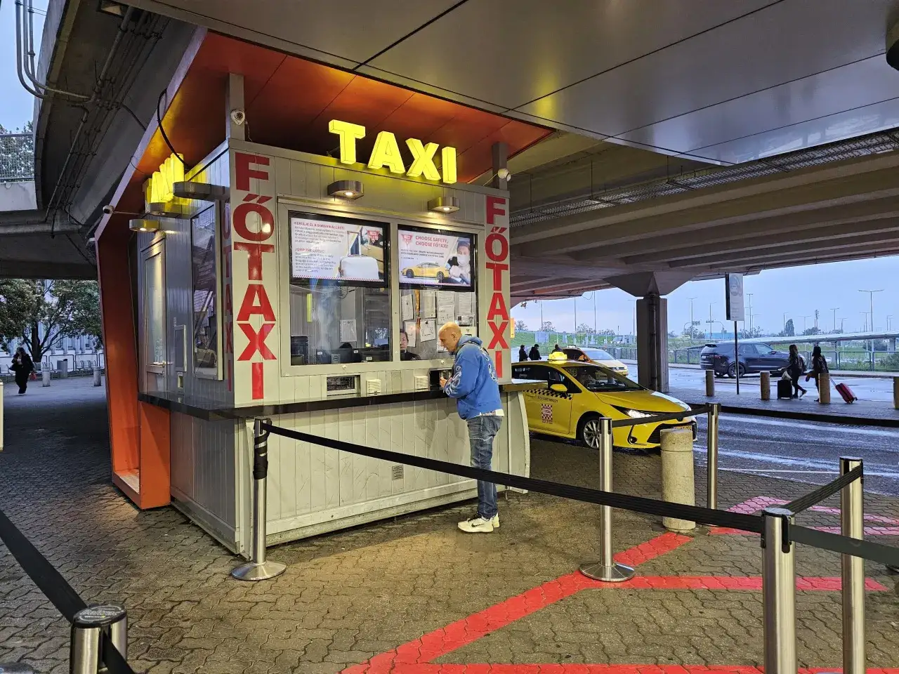 Postój Főtaxi na lotnisku Budapeszt im. Ferenca Liszta. Klient zamawia przejazd.