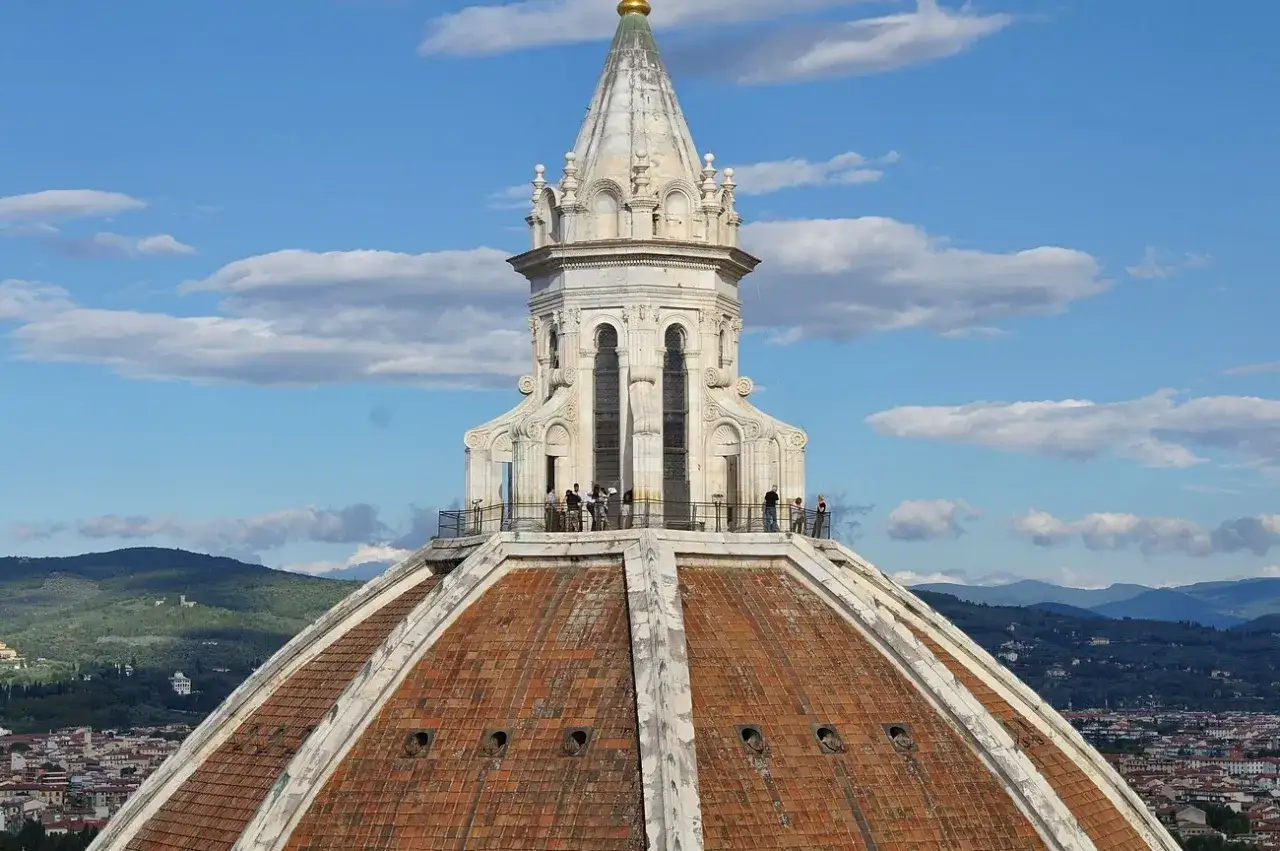 Widok na kopułę katedry Santa Maria del Fiore we Florencji. Kilku turystów podziwia panoramę miasta.