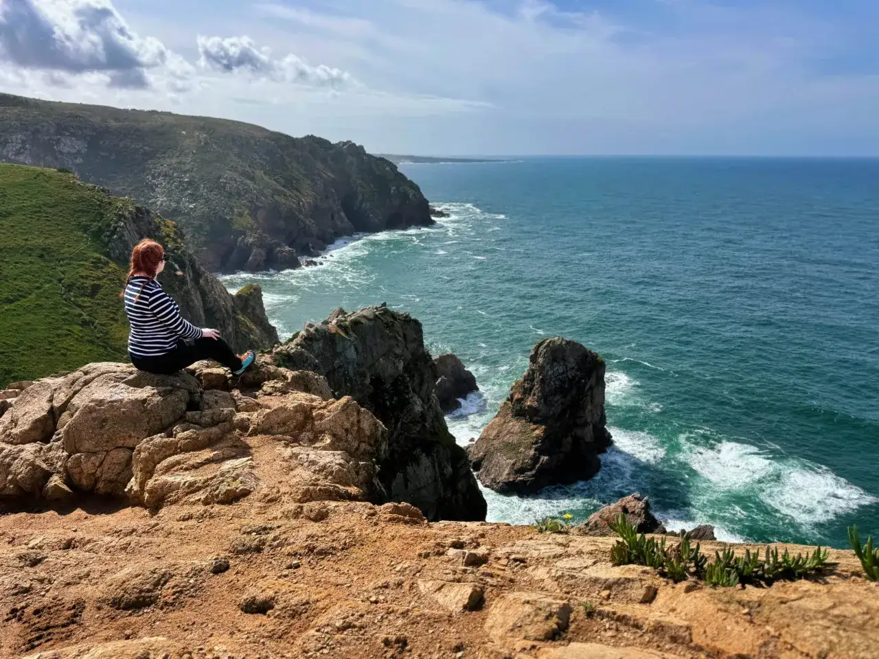 Kobieta z rudymi włosami siedzi na skale na Cabo da Roca, podziwiając ocean i klify.