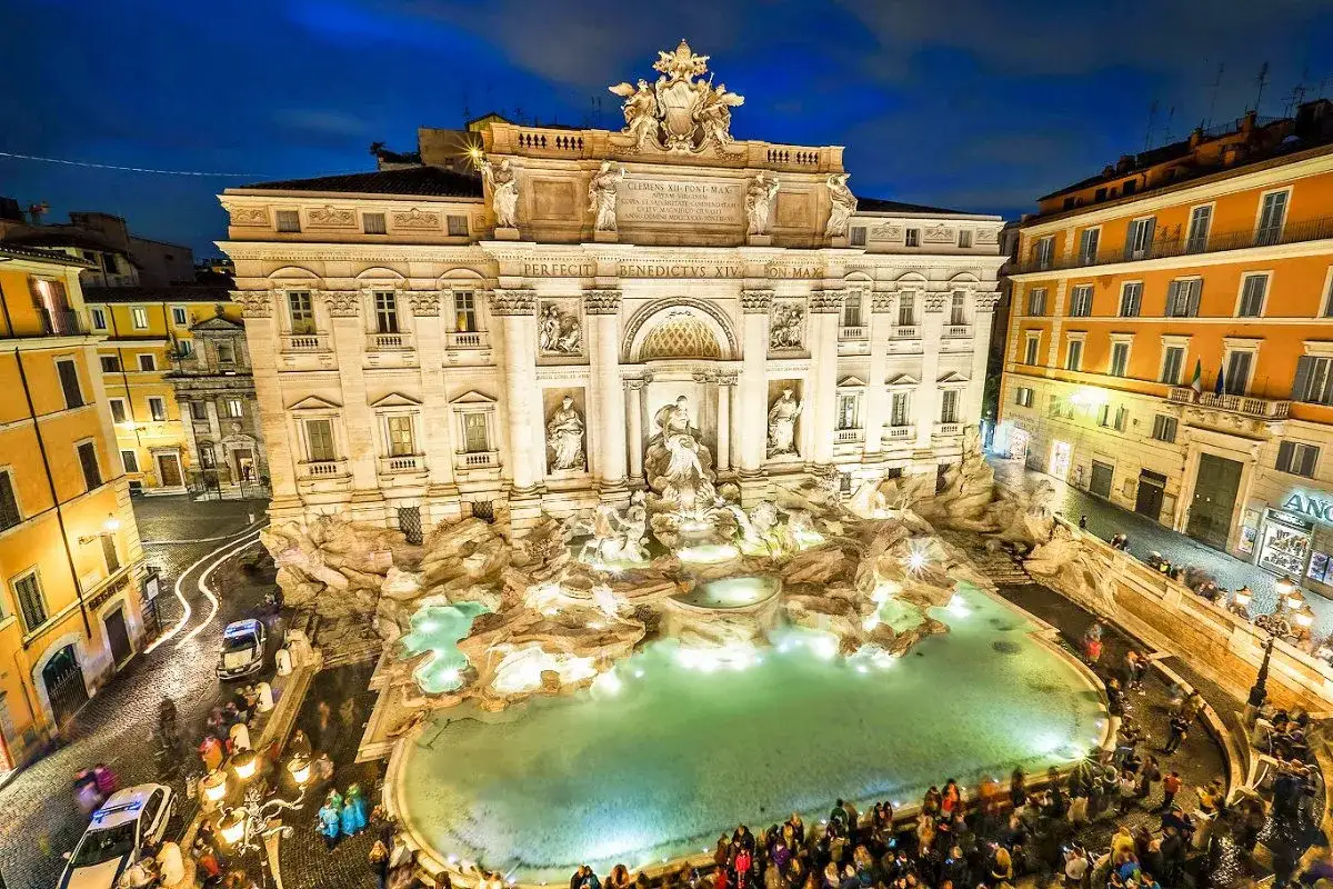 Nocna panorama Fontanny di Trevi w Rzymie, oświetlona i pełna turystów.
