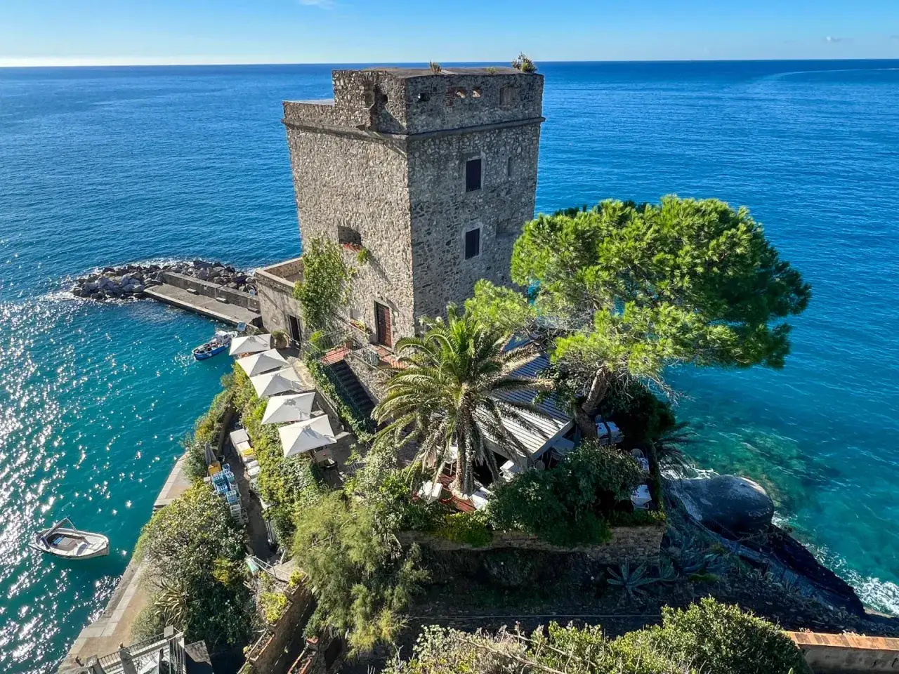 Kamienna wieża w Monterosso al Mare, otoczona zielenią i krystalicznie czystą wodą, z widokiem na morze.