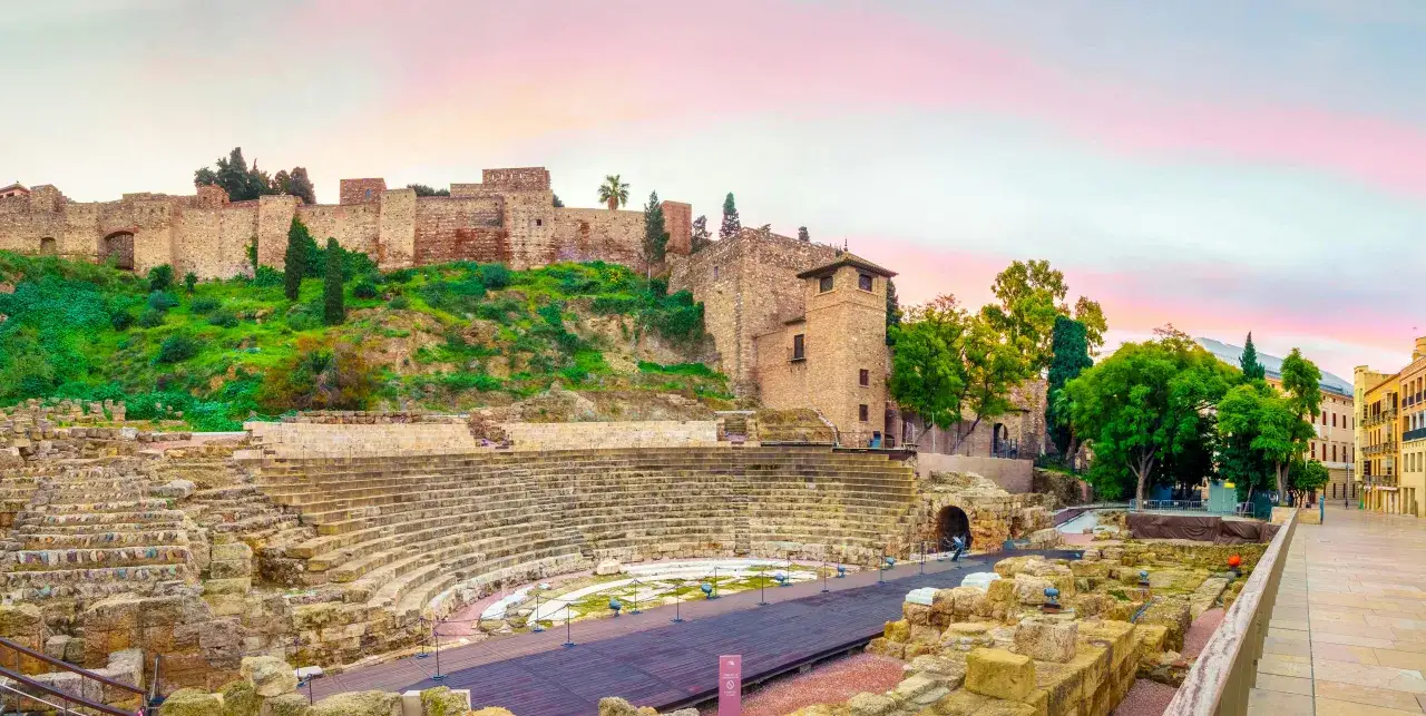 Malaga co zobaczyć: ruiny rzymskiego teatru i Alcazaba na wzgórzu, z pięknym niebem o zachodzie słońca.