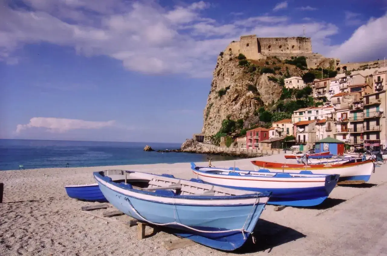 Łodzie na plaży w Reggio di Calabria, z widokiem na zamek na skale i kolorowe domy.