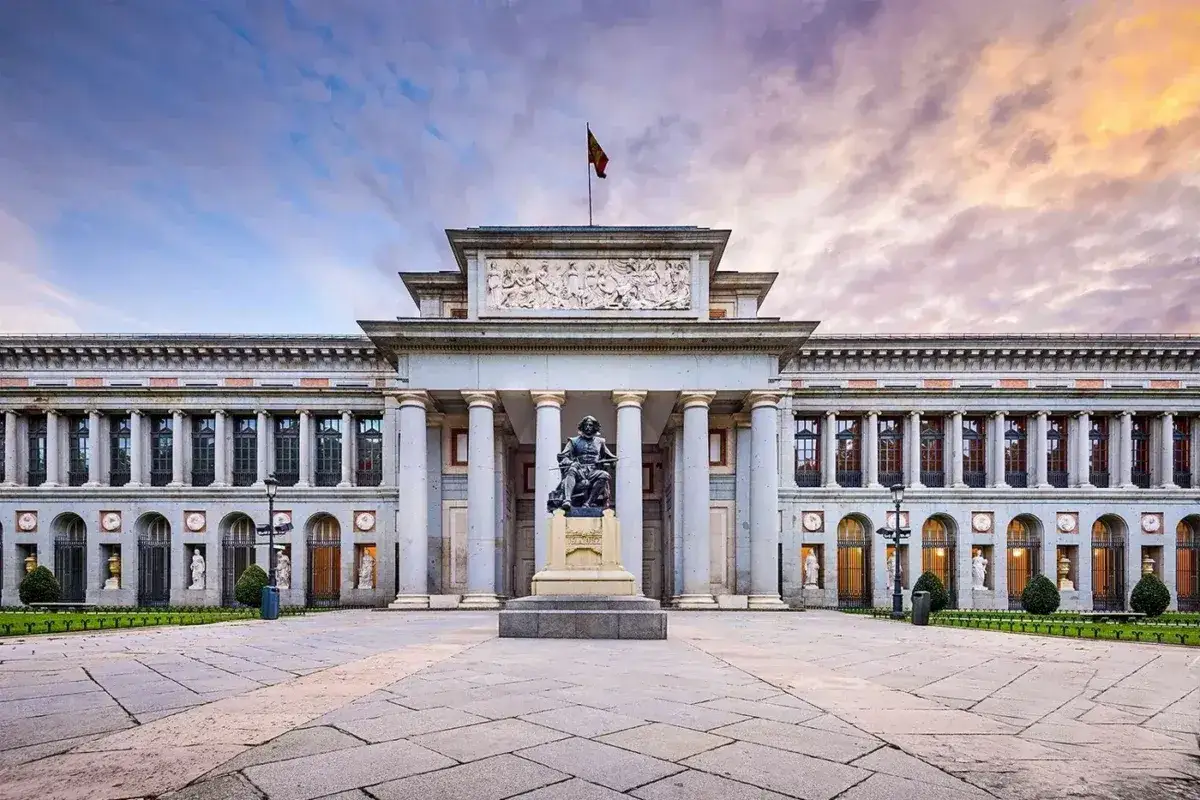 Prado, słynne muzeum w Madrycie, z pomnikiem przed fasadą i chmurami na niebie.