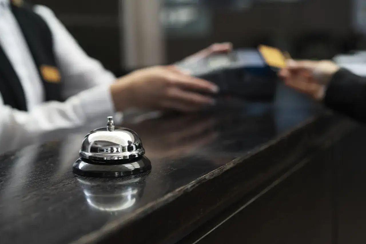 Dzwonek hotelowy i ręka podająca kartę płatniczą. Czy hotel ma prawo żądać dowodu osobistego? To pytanie często zadawane przy zameldowaniu.