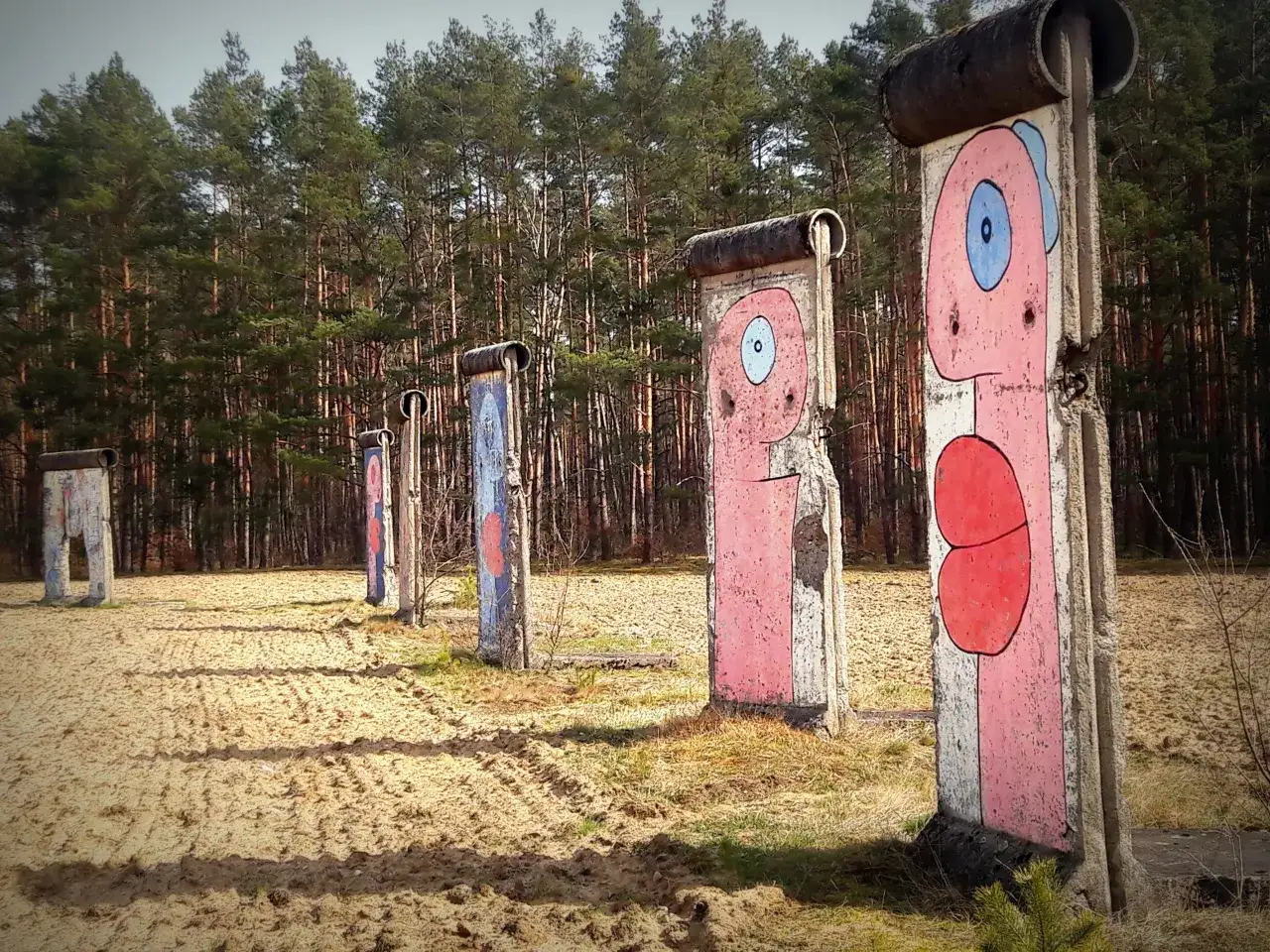 Fragment muru berlińskiego z kolorowymi, kreskówkowymi postaciami na tle lasu sosnowego.