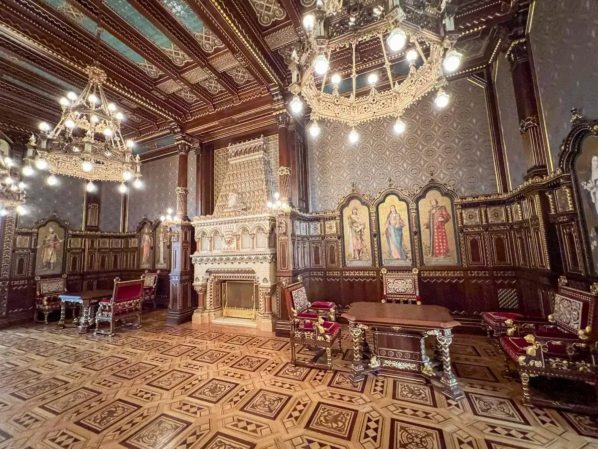 Bogato zdobione wnętrze, przypominające salę tronową w zamku królewskim w Budapeszcie, z kominkiem, mozaikami i ozdobnymi meblami.