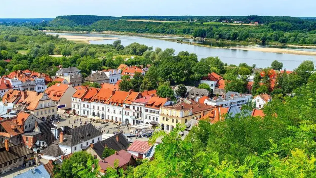 Widok na urokliwe stare miasto w Kazimierzu Dolnym z rzeką w tle. Dachy kamienic i zieleń tworzą malowniczy krajobraz.