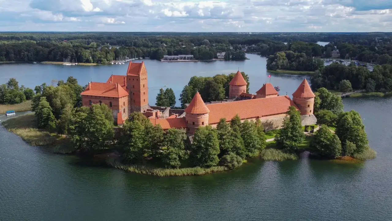 Zamek w Trokach, malowniczo położony na wyspie, otoczony wodą i zielenią.