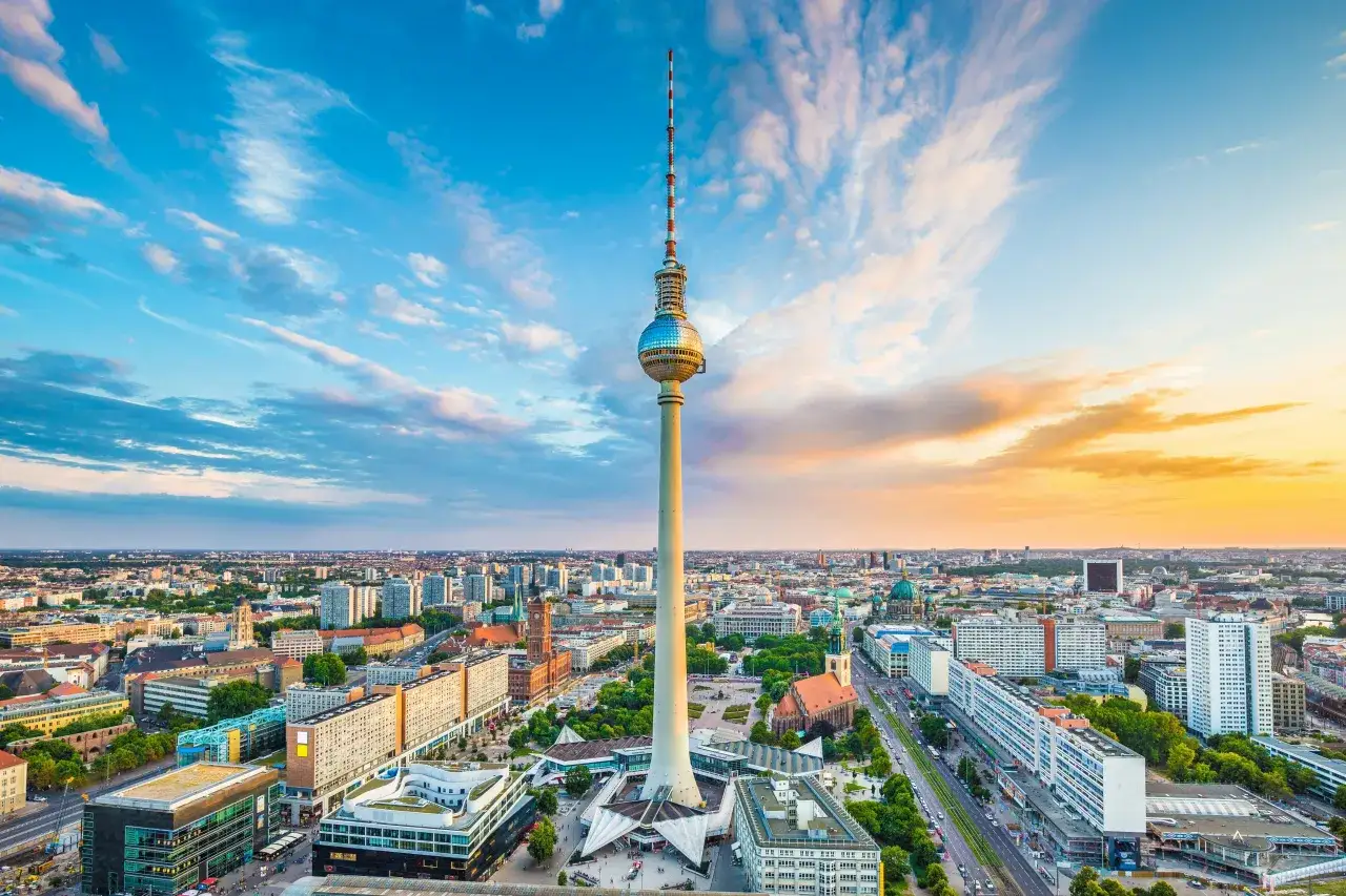 Wieża telewizyjna Berlin wznosi się nad miastem o zachodzie słońca, z chmurami malującymi niebo na złoto i różowo.