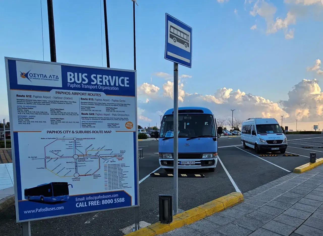 Tablica informacyjna z rozkładem jazdy autobusów na lotnisku Pafos. Obok parkujące busy.