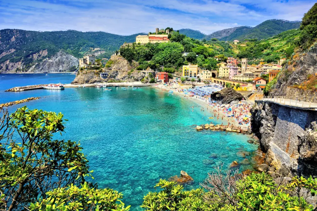 Słoneczna plaża w Monterosso al Mare, Liguria, Włochy. Turkusowa woda, kolorowe domy na wzgórzu, mnóstwo plażowiczów.