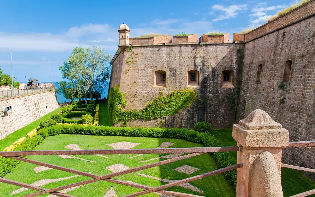 Zamek Castell de Montjuïc z zielonymi ogrodami i widokiem na morze.