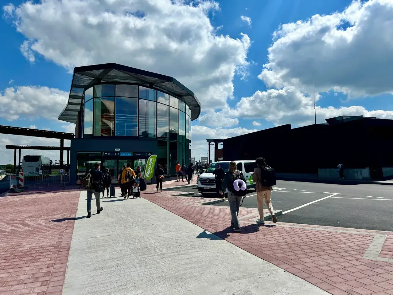 Ludzie z bagażami idą w stronę nowoczesnego budynku portu lotniczego Bruksela Charleroi.
