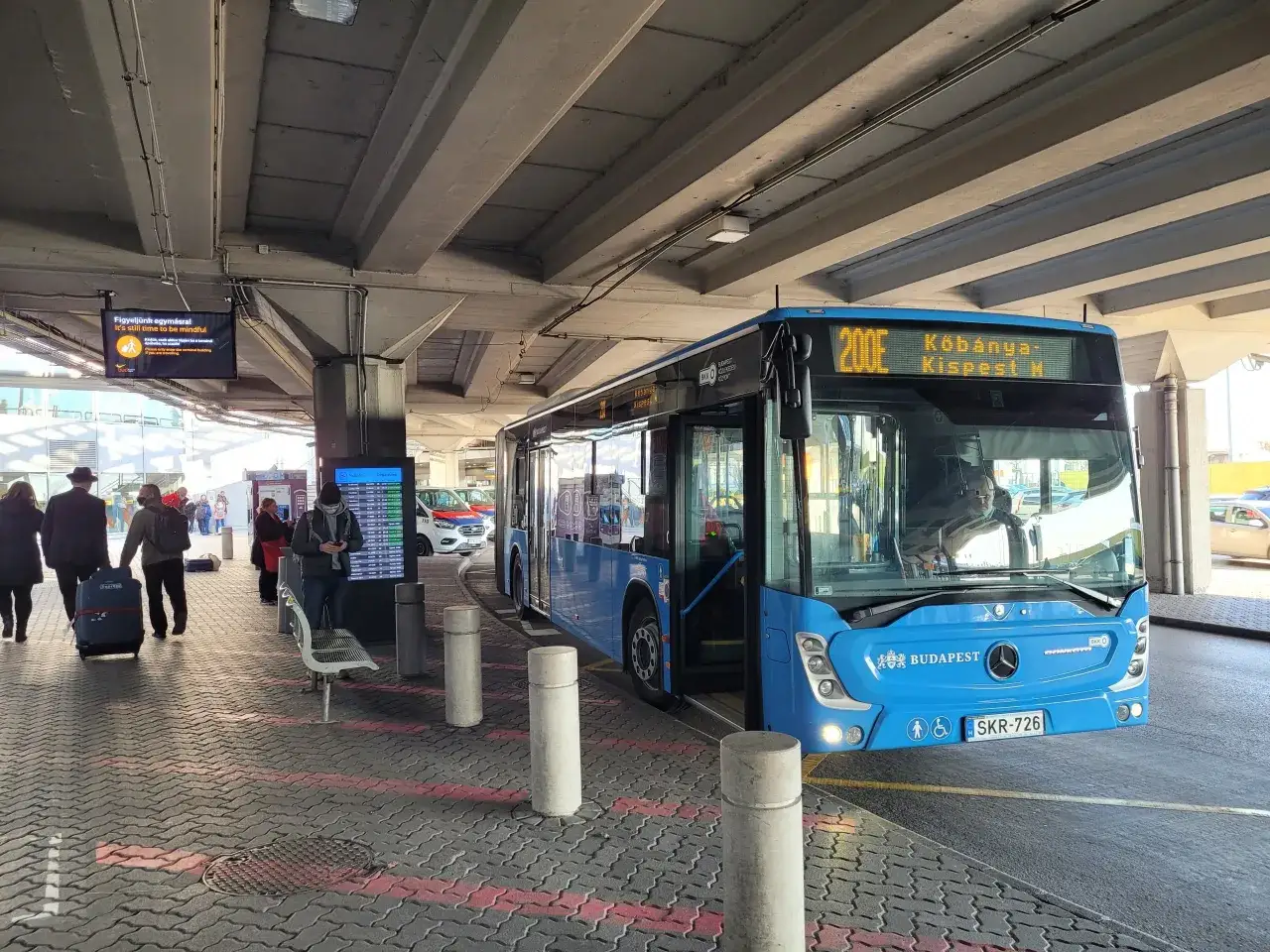 Autobus 200E na lotnisku Budapeszt im. Ferenca Liszta. Pasażerowie z bagażami czekają na odjazd.