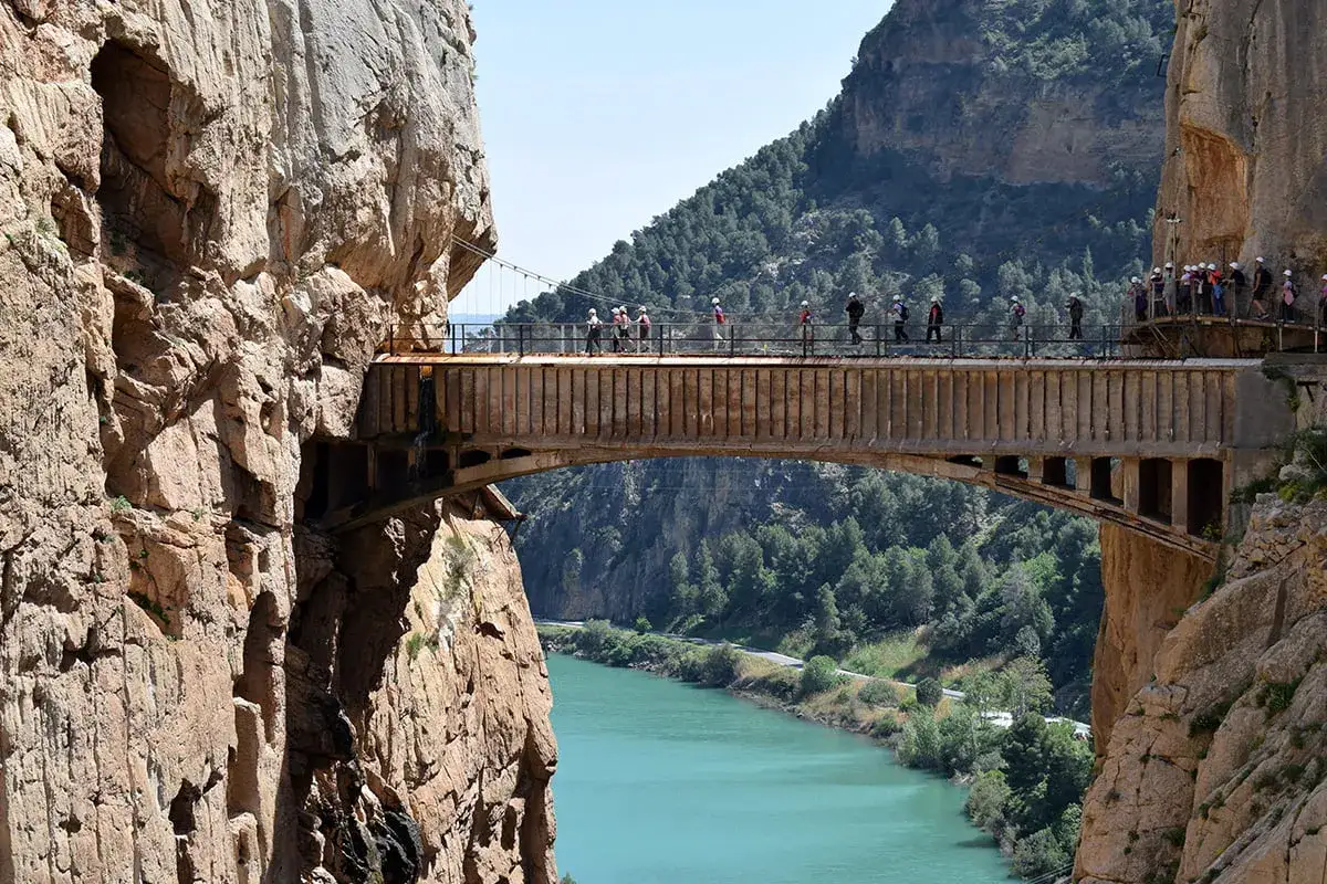 Mostek na Camino del Rey, jedna z głównych atrakcji, które warto zobaczyć w Maladze. Turyści spacerują po wąskiej ścieżce zawieszonej nad turkusową rzeką.