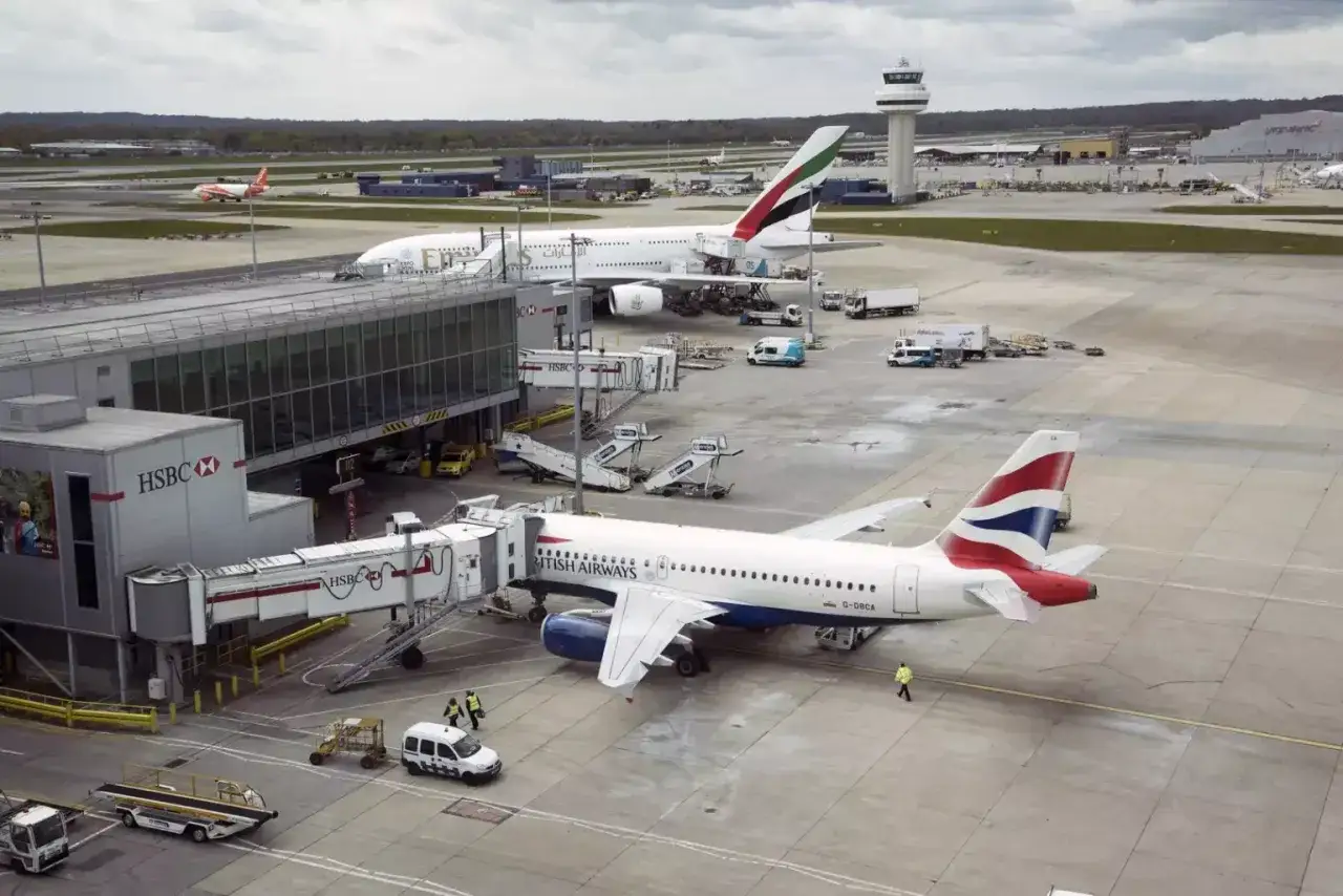 Samoloty British Airways i Emirates na płycie postojowej portu lotniczego Londyn Gatwick. W tle wieża kontroli lotów.