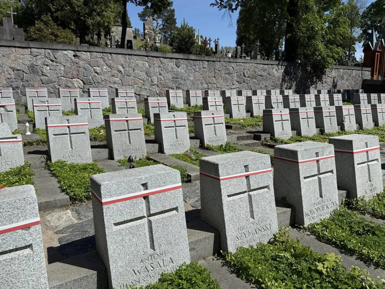 Rzędy identycznych nagrobków z krzyżami i biało-czerwonymi wstęgami tworzą porządek na cmentarzu na Rossie.
