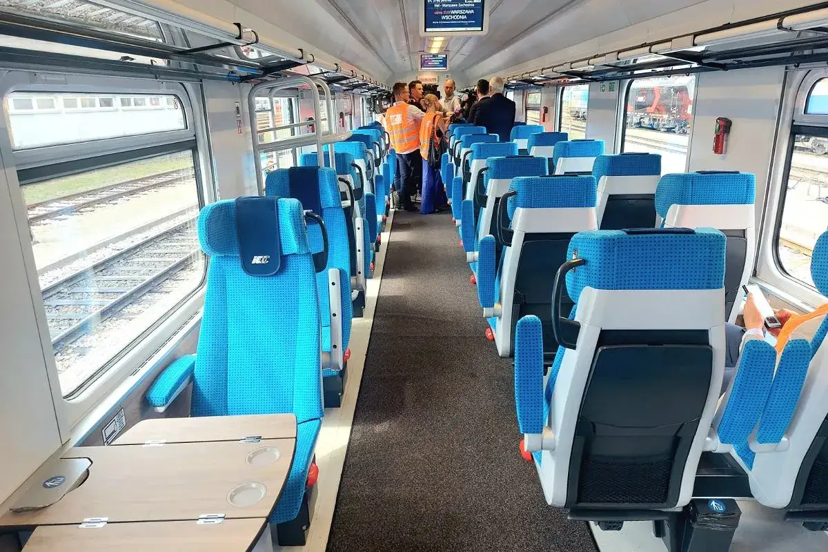 Wnętrze Pendolino z Krakowa do Warszawy. Siedzenia w kolorze niebieskim, stoliki, okna z widokiem na tory.