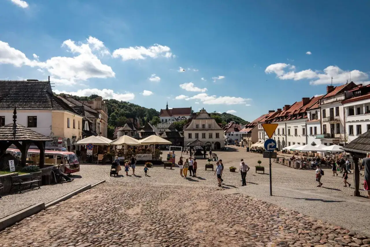 Kazimierz Dolny atrakcje: Rynek tętni życiem, z ludźmi spacerującymi między kamienicami i ogródkami kawiarnianymi.