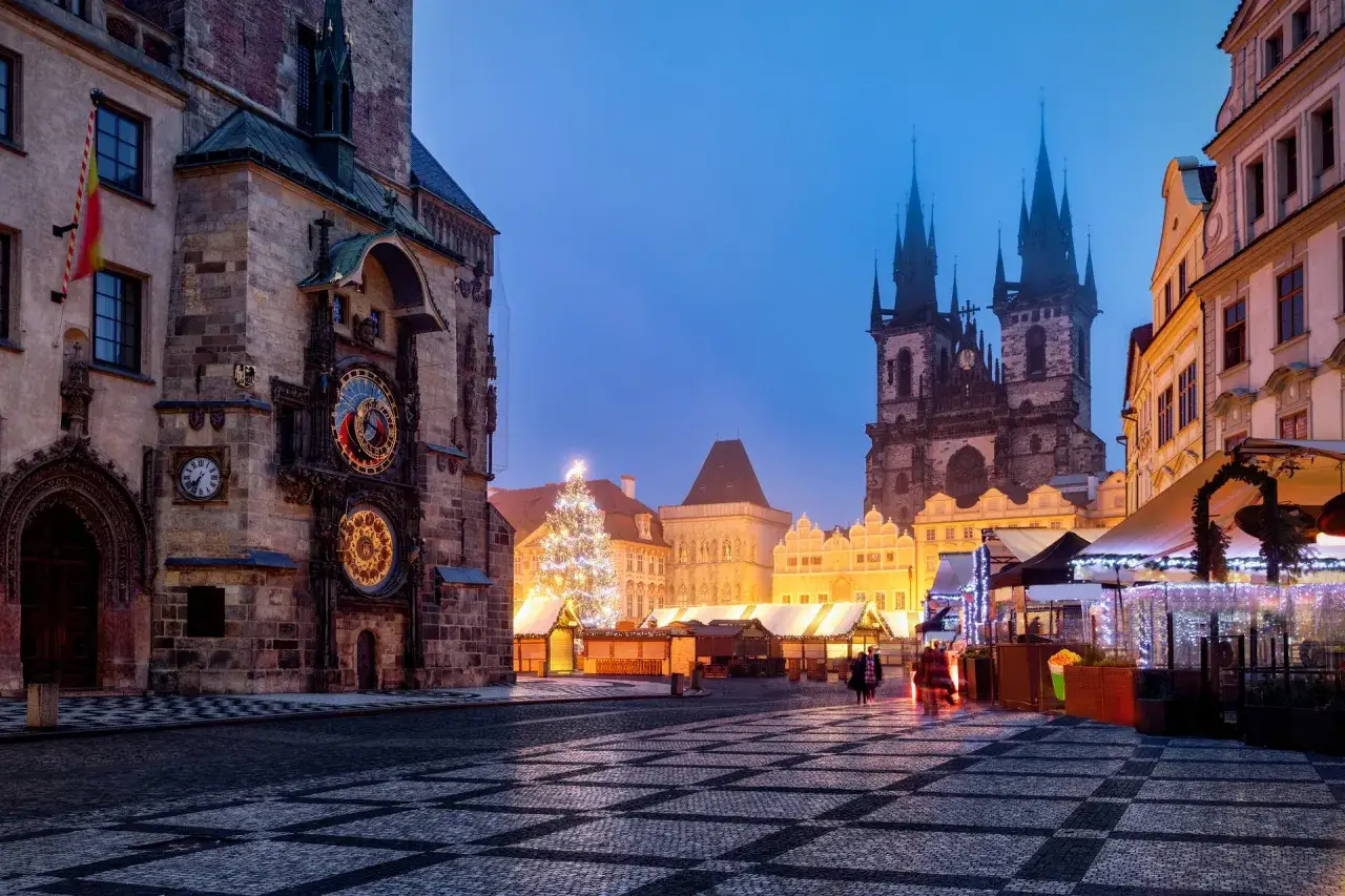 Rynek Staromiejski w Pradze nocą, z oświetloną choinką i jarmarkiem świątecznym. Widoczny zegar astronomiczny.