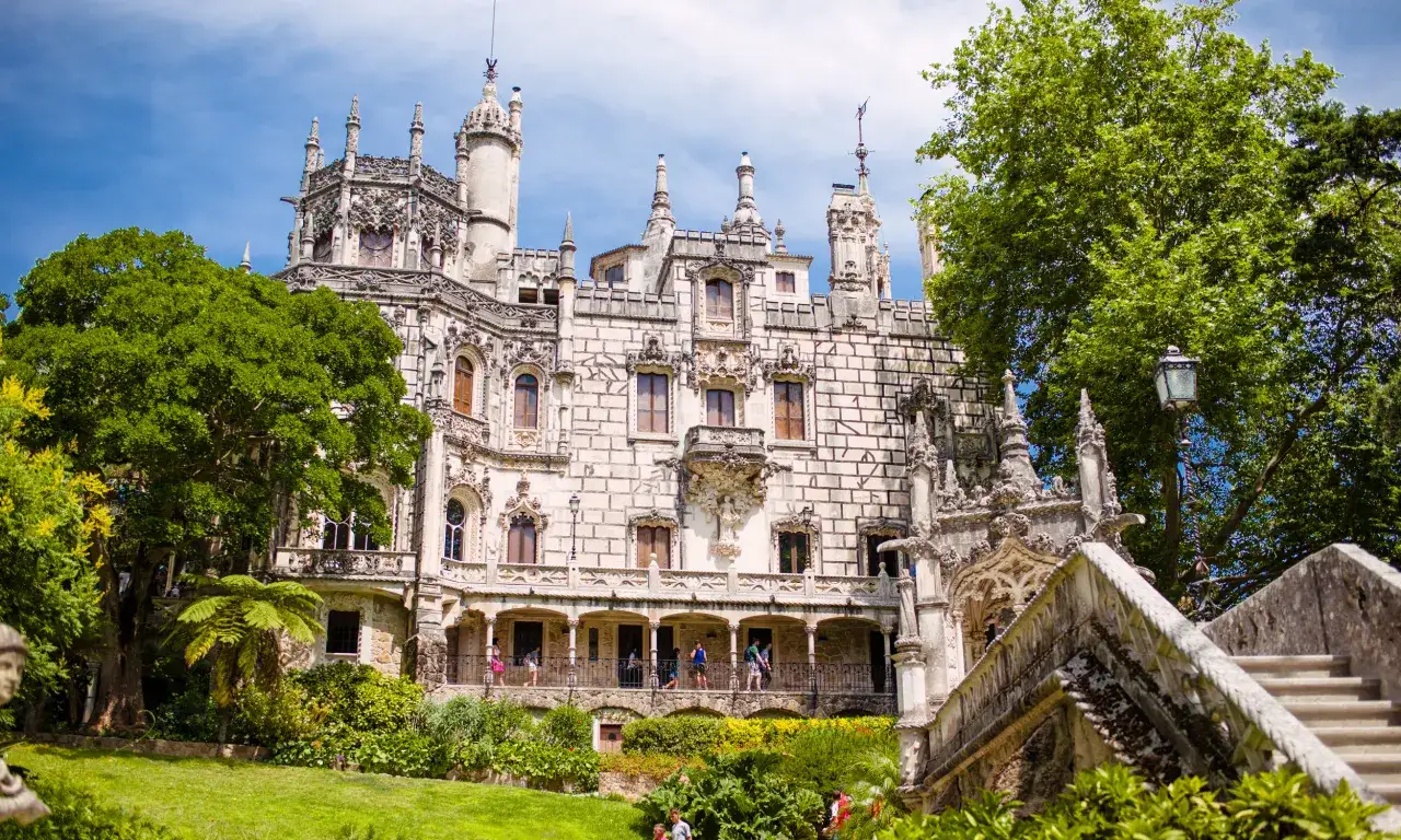Majestatyczny pałac Quinta da Regaleira z bogato zdobioną fasadą, otoczony bujną zielenią i błękitnym niebem.