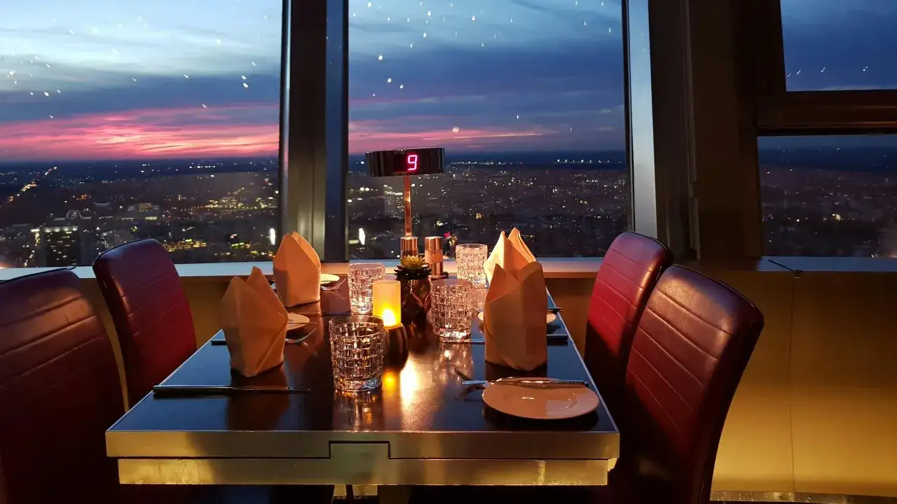 Stolik w restauracji na szczycie wieży telewizyjnej w Berlinie, z widokiem na miasto o zachodzie słońca.