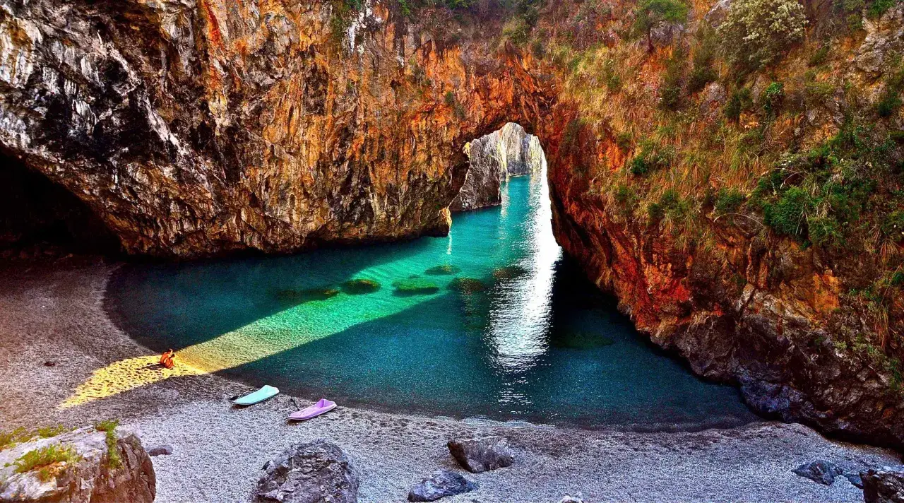 Malownicza zatoczka z turkusową wodą i łodziami, ukryta w skalnym łuku. Rajskie miejsce w Reggio di Calabria.