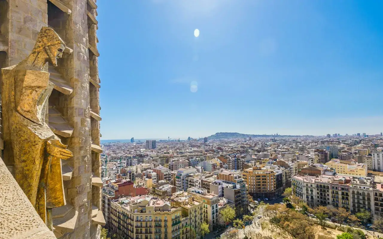 Złota rzeźba na tle panoramy Barcelony, z widokiem na miasto i morze. To fragment La Sagrada Familia, arcydzieła Gaudiego.