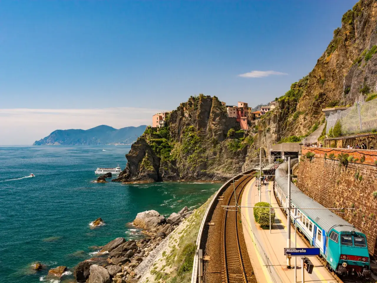 Pociąg na stacji Manarola w Cinque Terre, prowincja La Spezia, Włochy. Kolorowe domy wznoszą się na klifie nad turkusowym morzem.