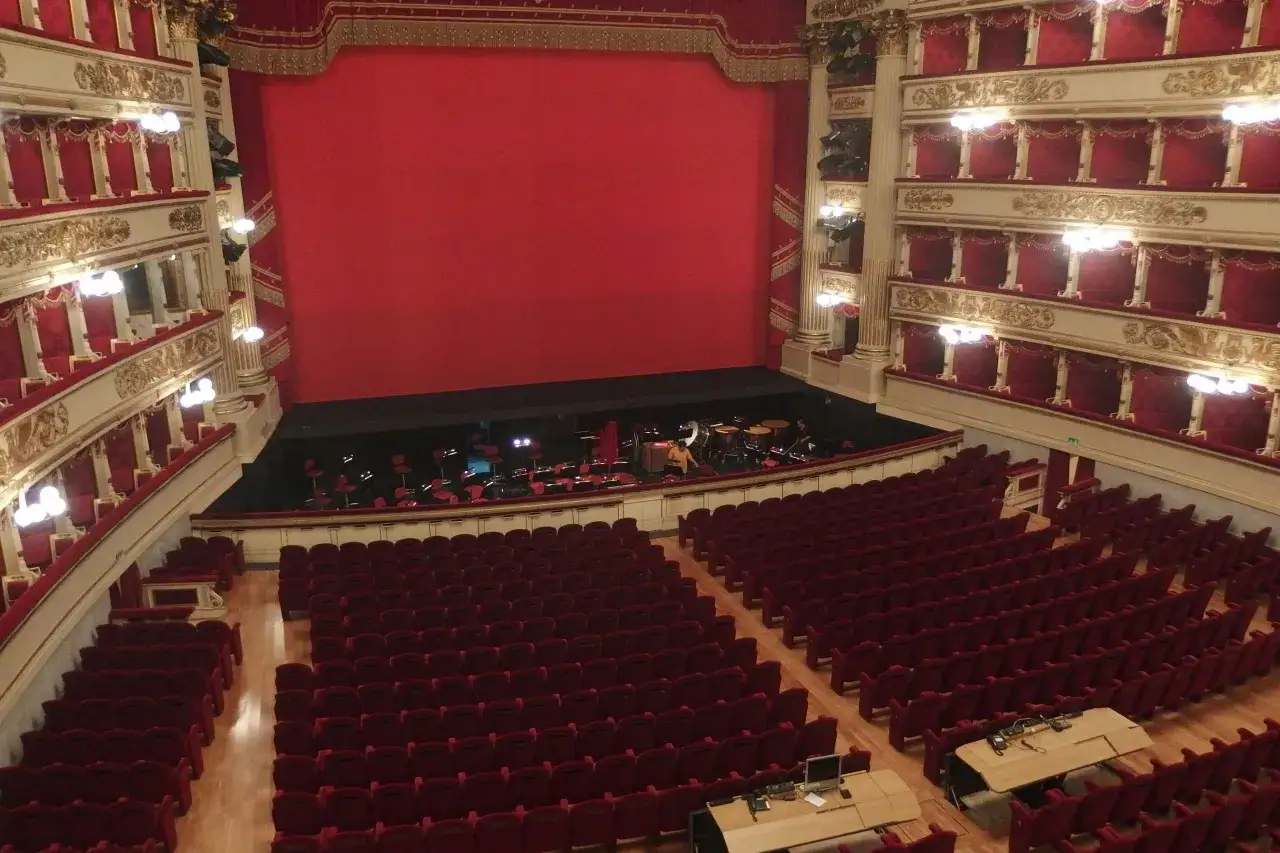 Wnętrze La Scala w Mediolanie: czerwone fotele, złote zdobienia i scena z instrumentami.
