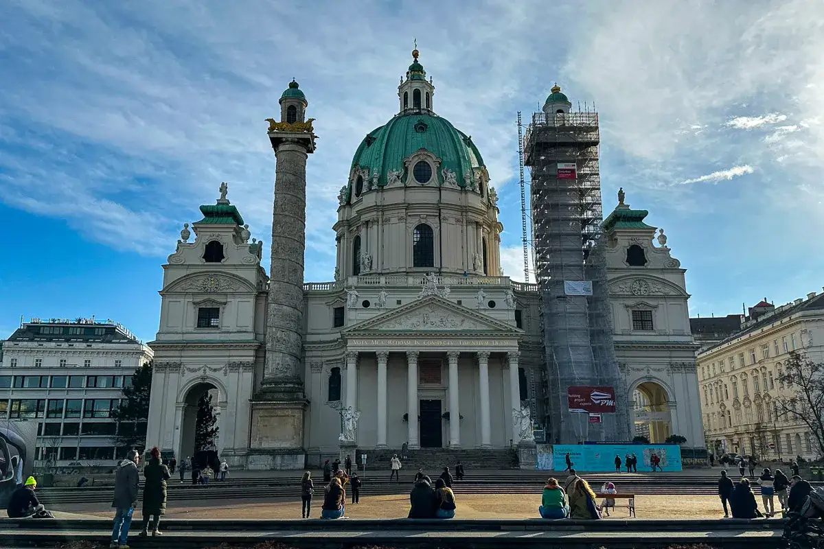Majestatyczny kościół św. Karola w Wiedniu z zieloną kopułą i kolumną. Część budowli w rusztowaniach.