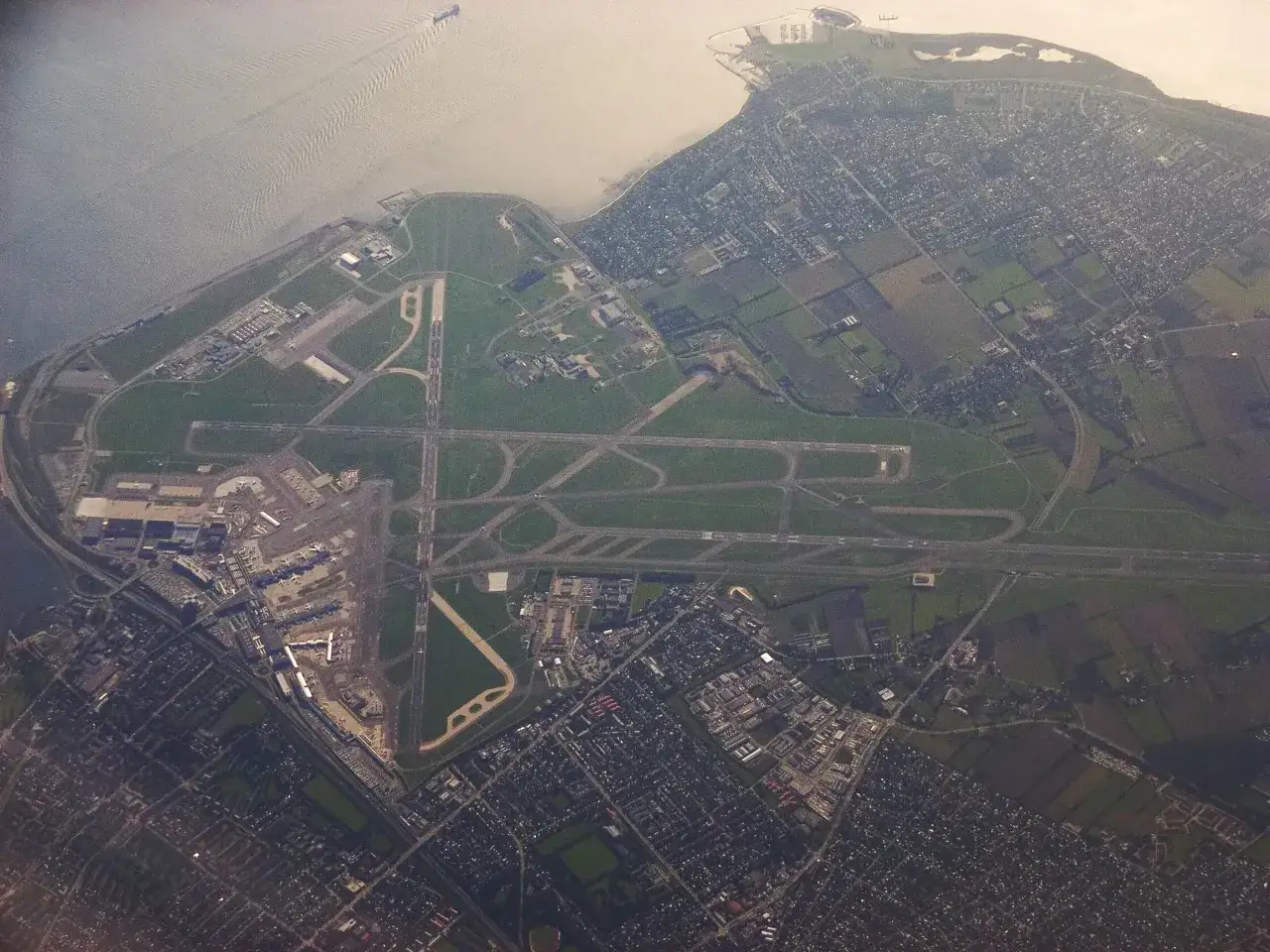 Widok z lotu ptaka na port lotniczy Kopenhaga Kastrup z licznymi pasami startowymi, budynkami terminali i otaczającą zabudową mieszkalną.