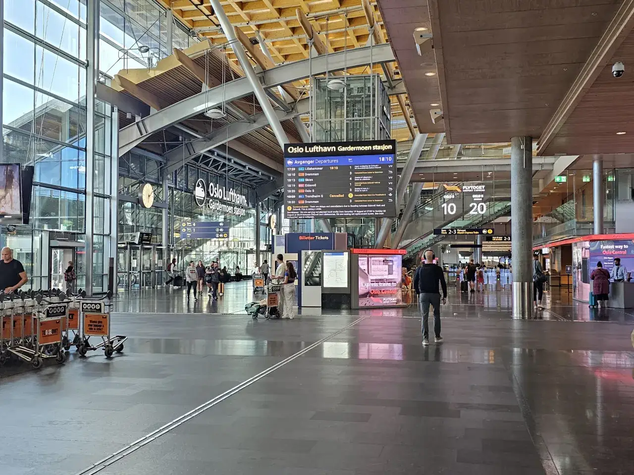 Wnętrze portu lotniczego Oslo Gardermoen z tablicą odlotów i podróżnymi.