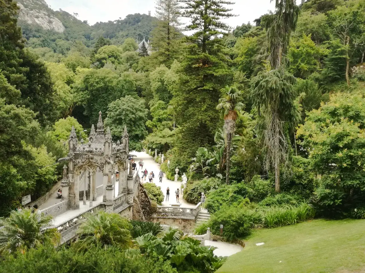 Malowniczy park Quinta da Regaleira z kamiennymi mostkami, rzeźbami i bujną zielenią.