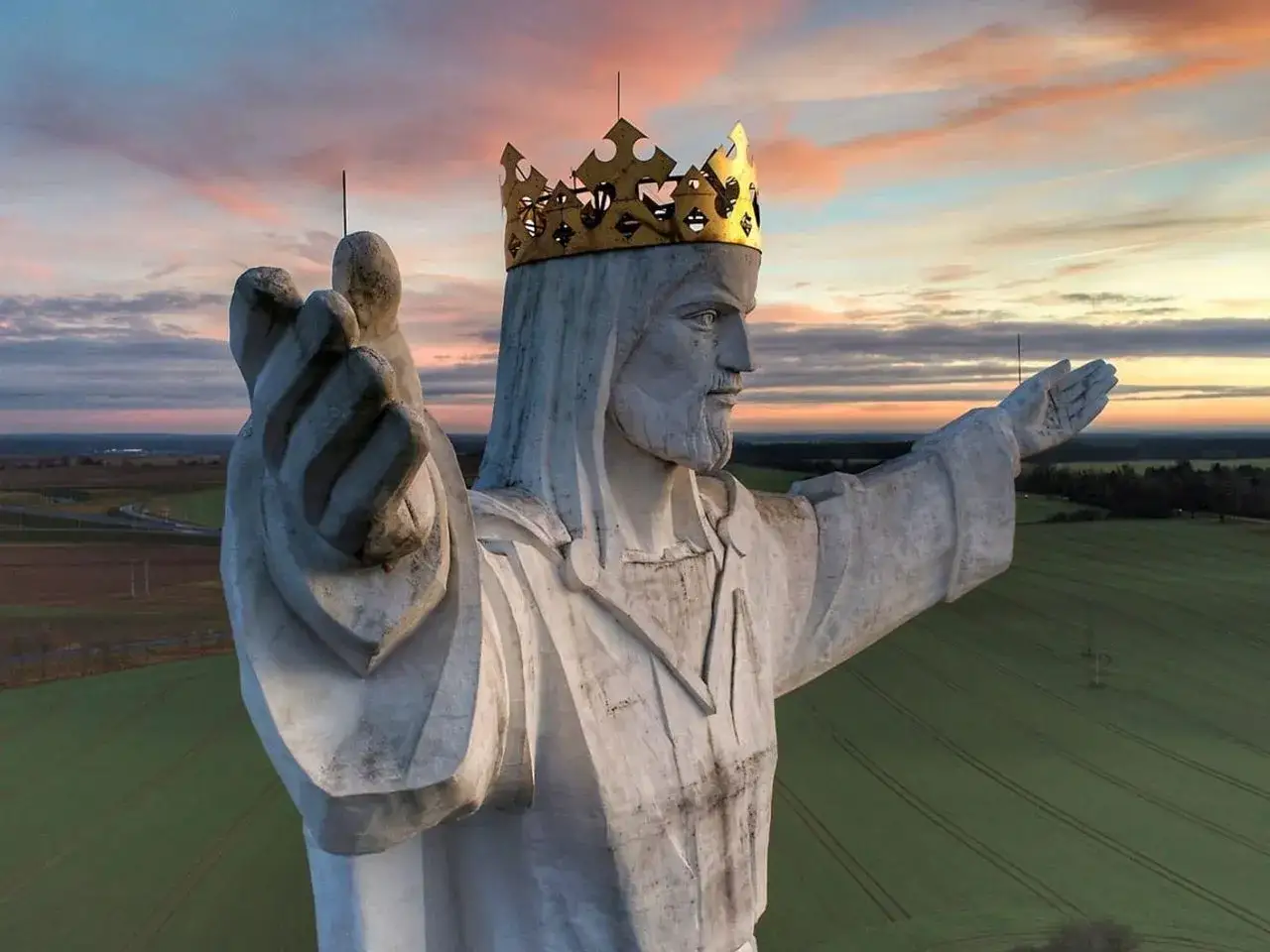 Majestatyczny pomnik Jezusa w koronie, jeden z wielu pomników Jezusa w Polsce, wznosi się nad polami o zachodzie słońca.