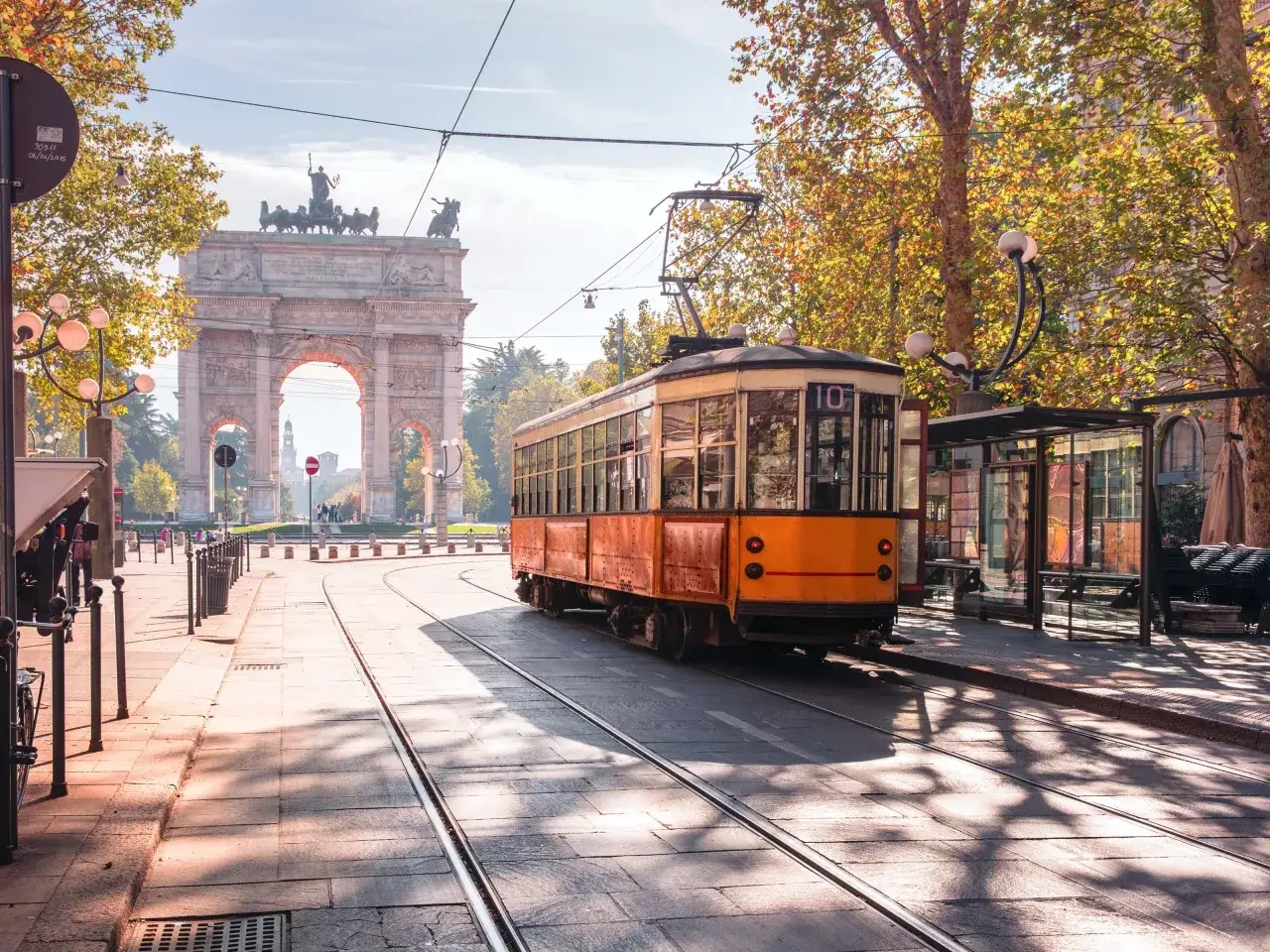 Mediolan co zobaczyć: zabytkowy tramwaj i Łuk Pokoju na tle jesiennych drzew.