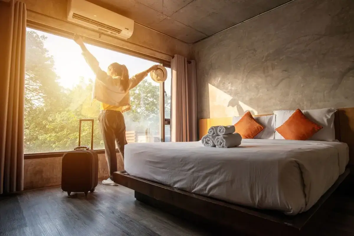 Kobieta z walizką wita nowy dzień w pokoju hotelowym. Idealne miejsce, gdzie szukać noclegu na wakacje.