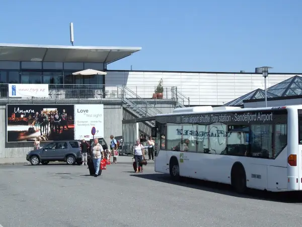 Autobus wahadłowy na lotnisku Sandefjord Torp. Ludzie z bagażami czekają na transport.