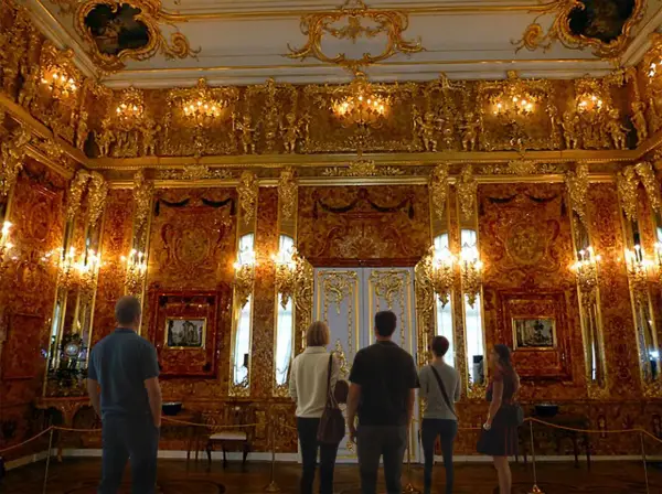 Grupa turystów podziwia bogactwo bursztynowej komnaty w Mamerkach. Złote zdobienia i bursztynowe panele tworzą niezwykły blask.